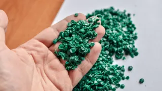 A close up photo of a hand holding up green recycled plastic chips.