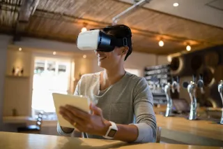 A photo of a person wearing a virtual reality headset is holding a tablet.