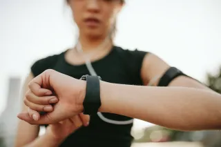A jogger wearing headphones is looking at her watch.
