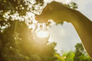 Photo of a hand holding a lightbulb in front of a sunset, symbolising clean energy.