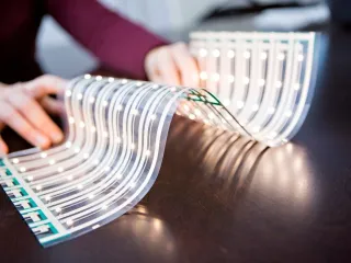 A piece of bent, flexible LED foil is illuminated and laid out on a table
