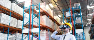 A photo of a person wearing a hard hat and a virtual reality headset in a warehouse.