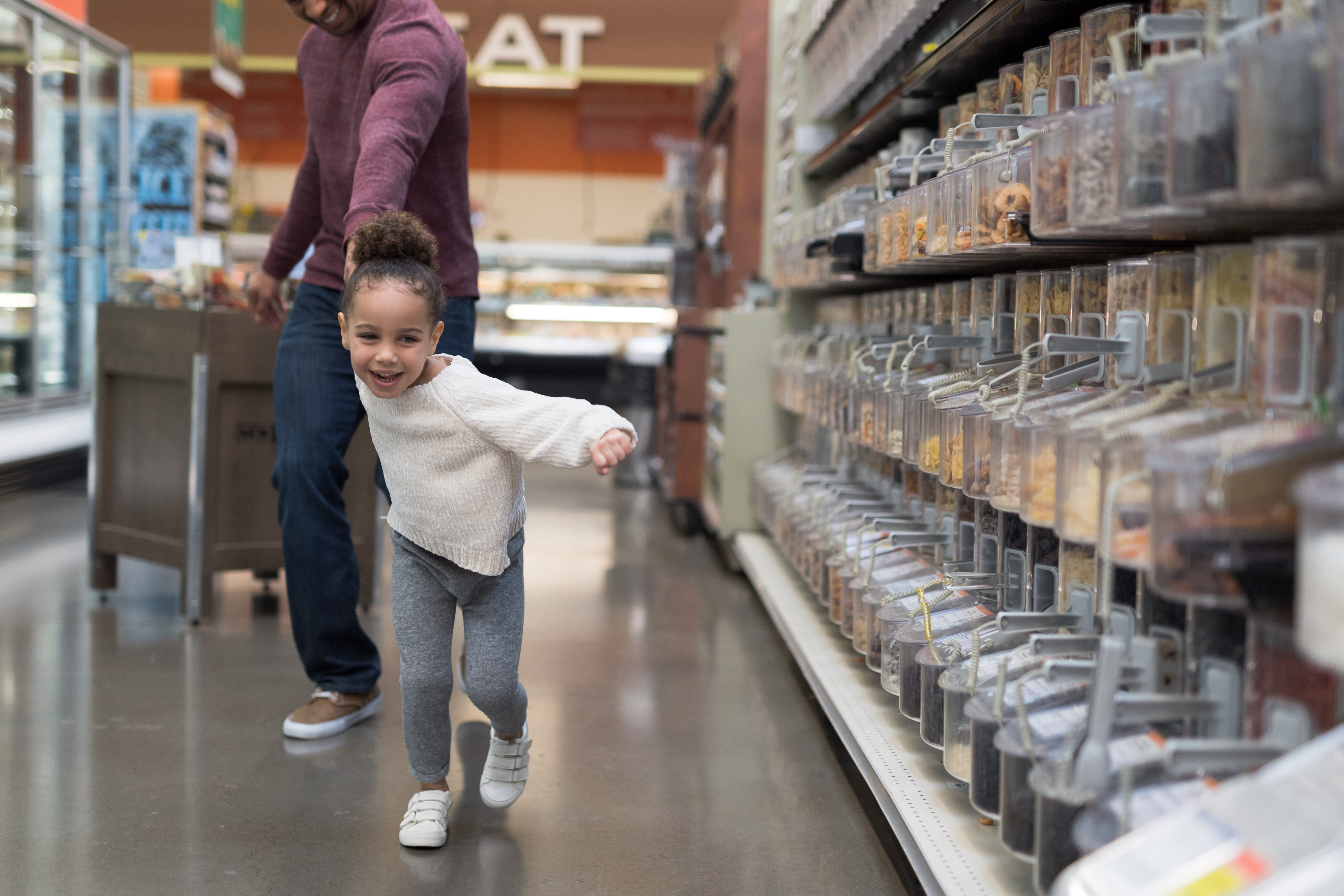 A child is excitedly pulling their parent towards the candy aisle inside a grocery store