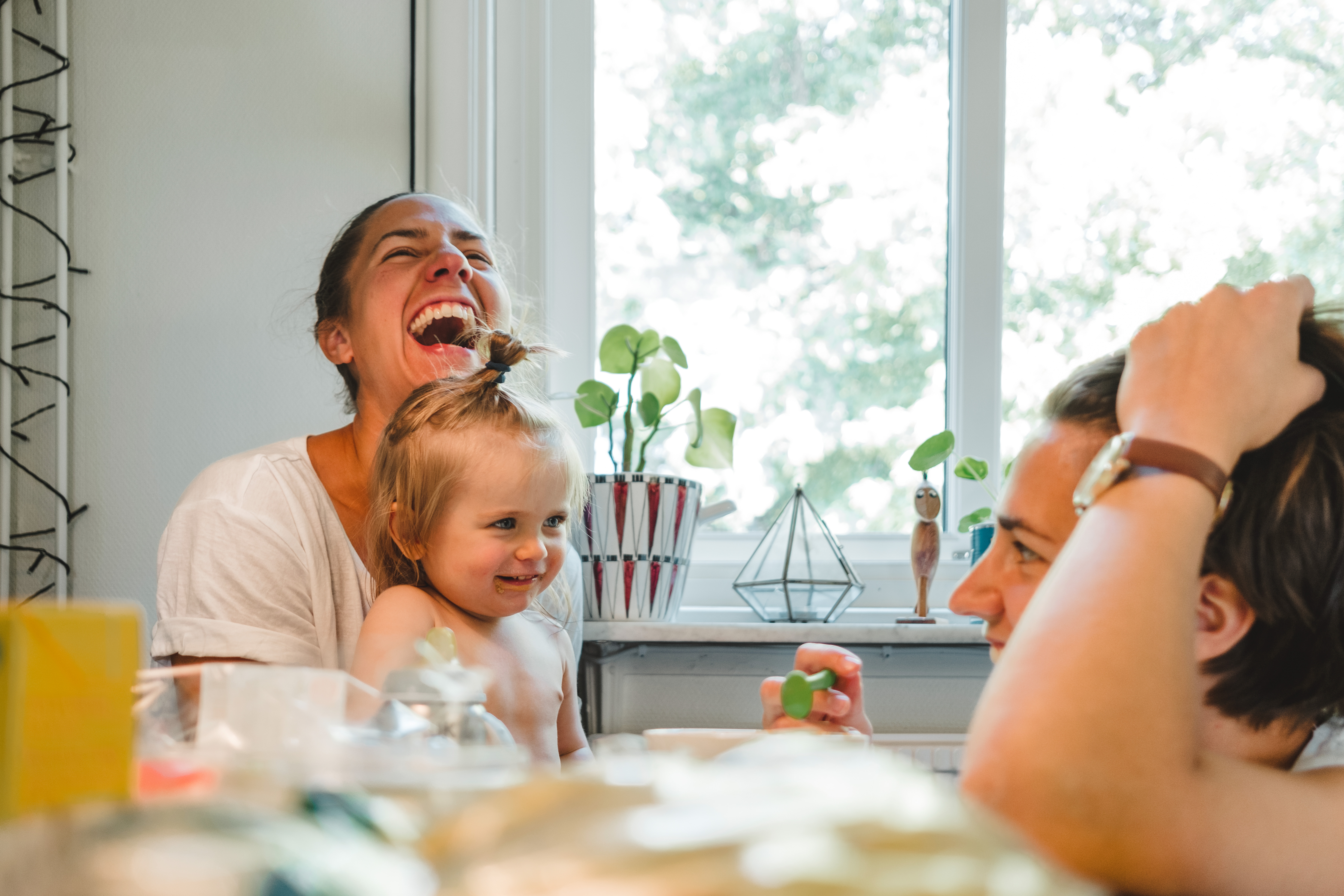 A family of two adults and a small child are sitting in the kitchen, laughing