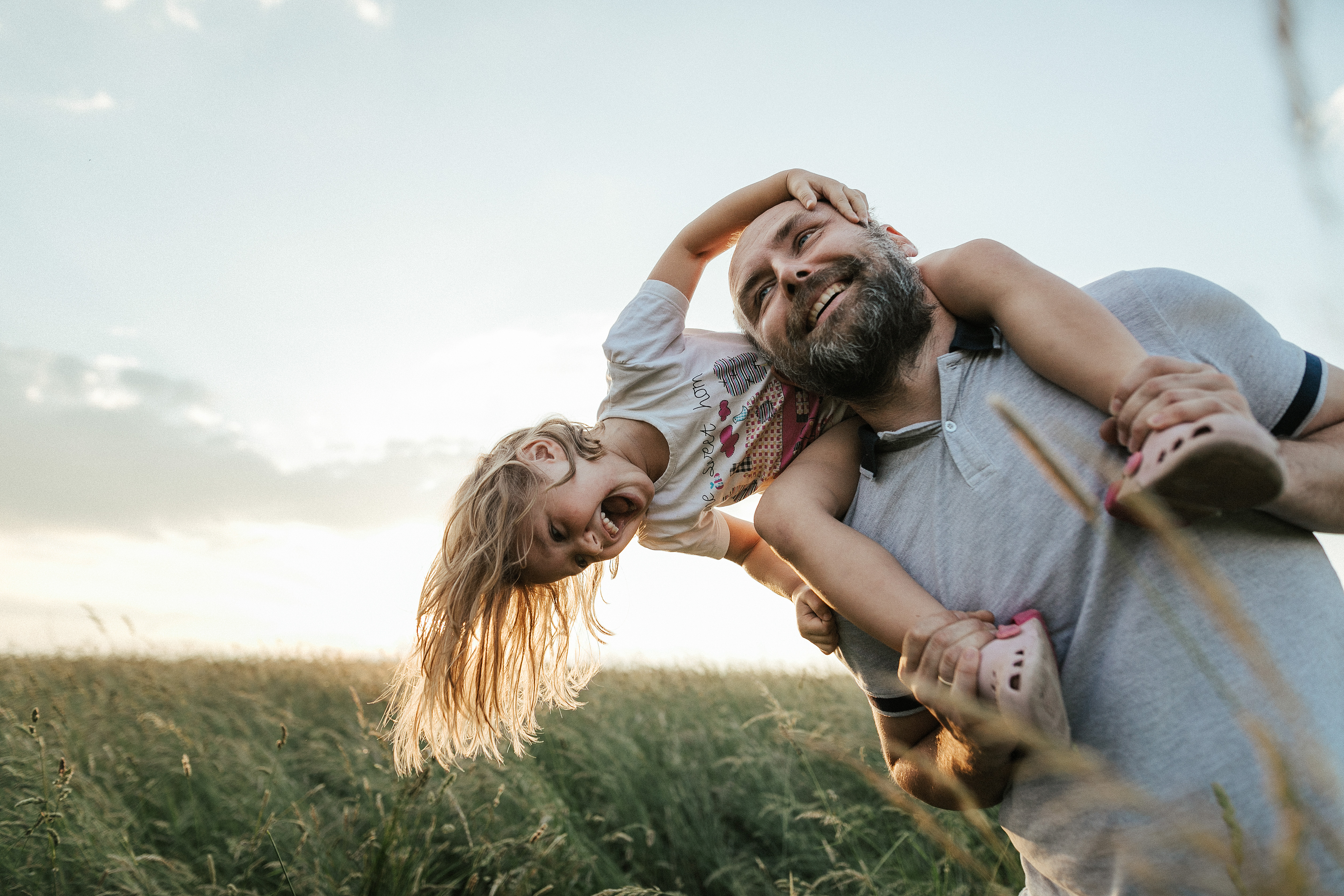 A girl is sitting on her father&#039;s shoulders, playing and laughing in a field at sunset