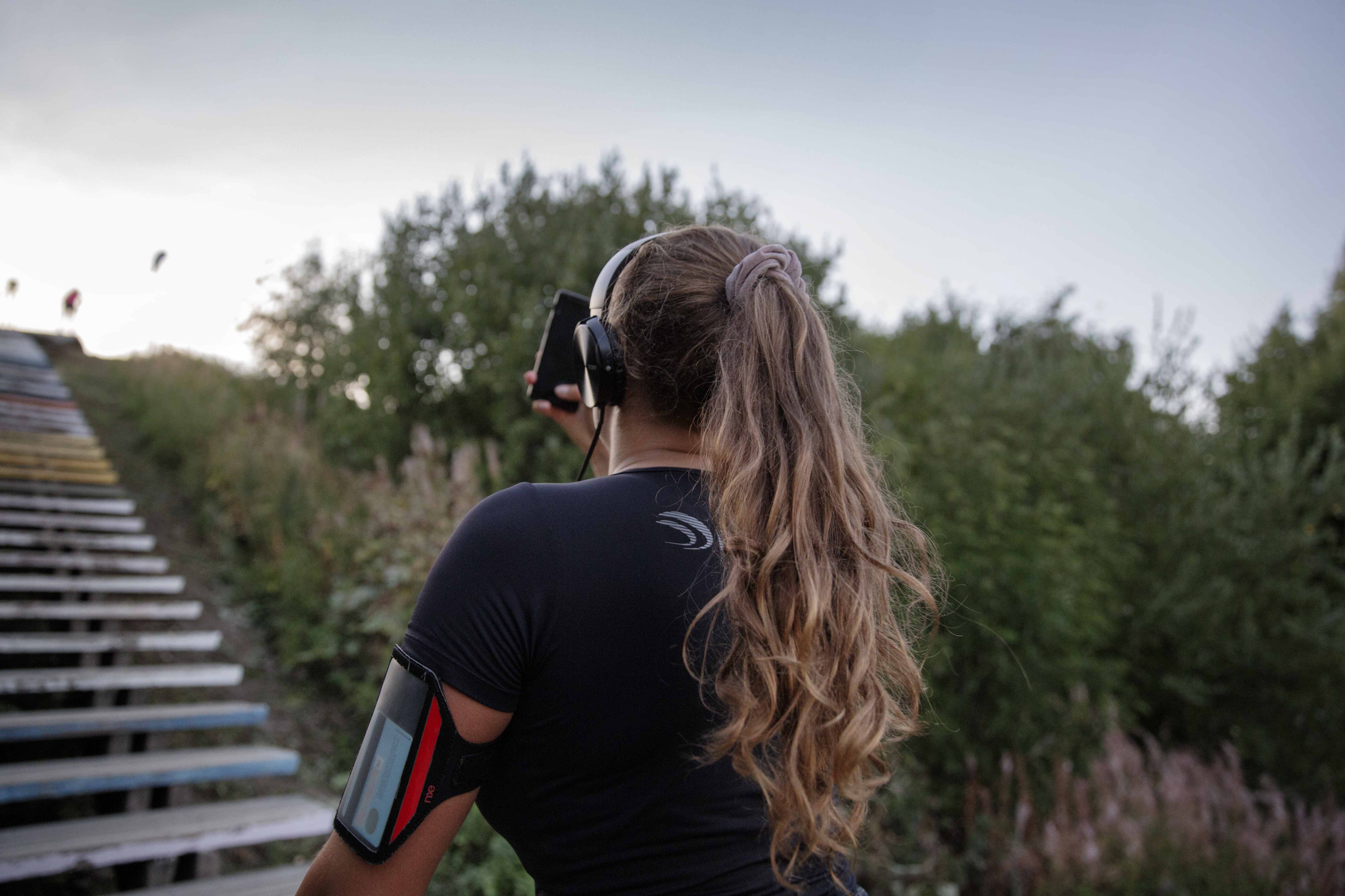 A sporty jogger is running up a set of stairs on a hill and is holding a mobile device