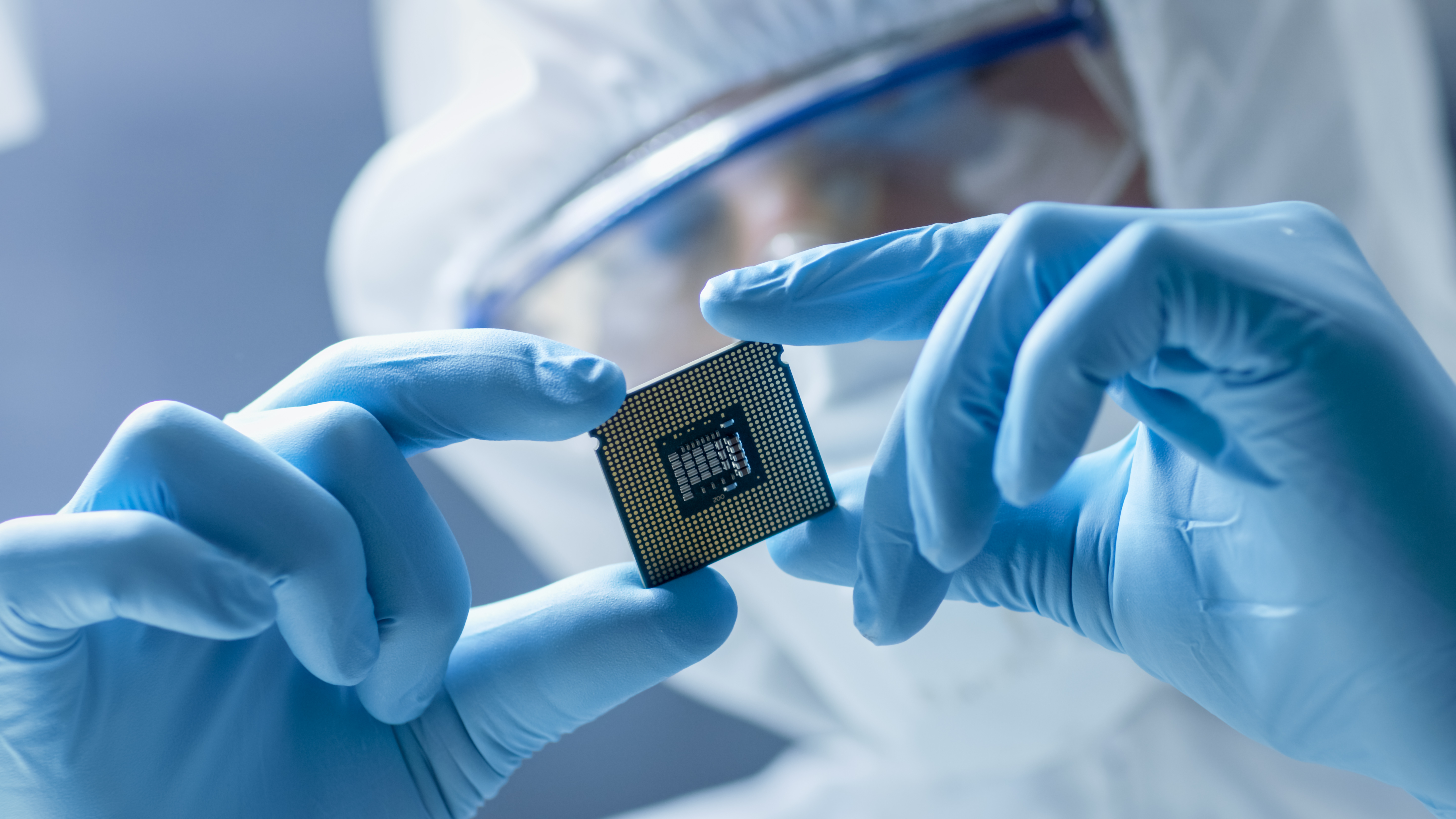 A photo of a person wearing rubber gloves, a face guard and protective overalls examining a microchip.