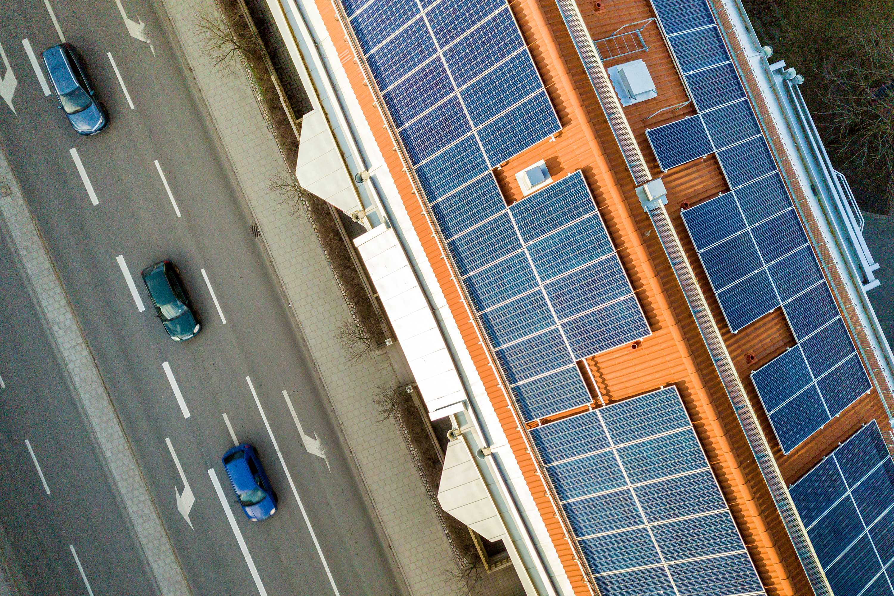 An aerial photo of a building next to a street. The building has solar panels covering the entire roof.