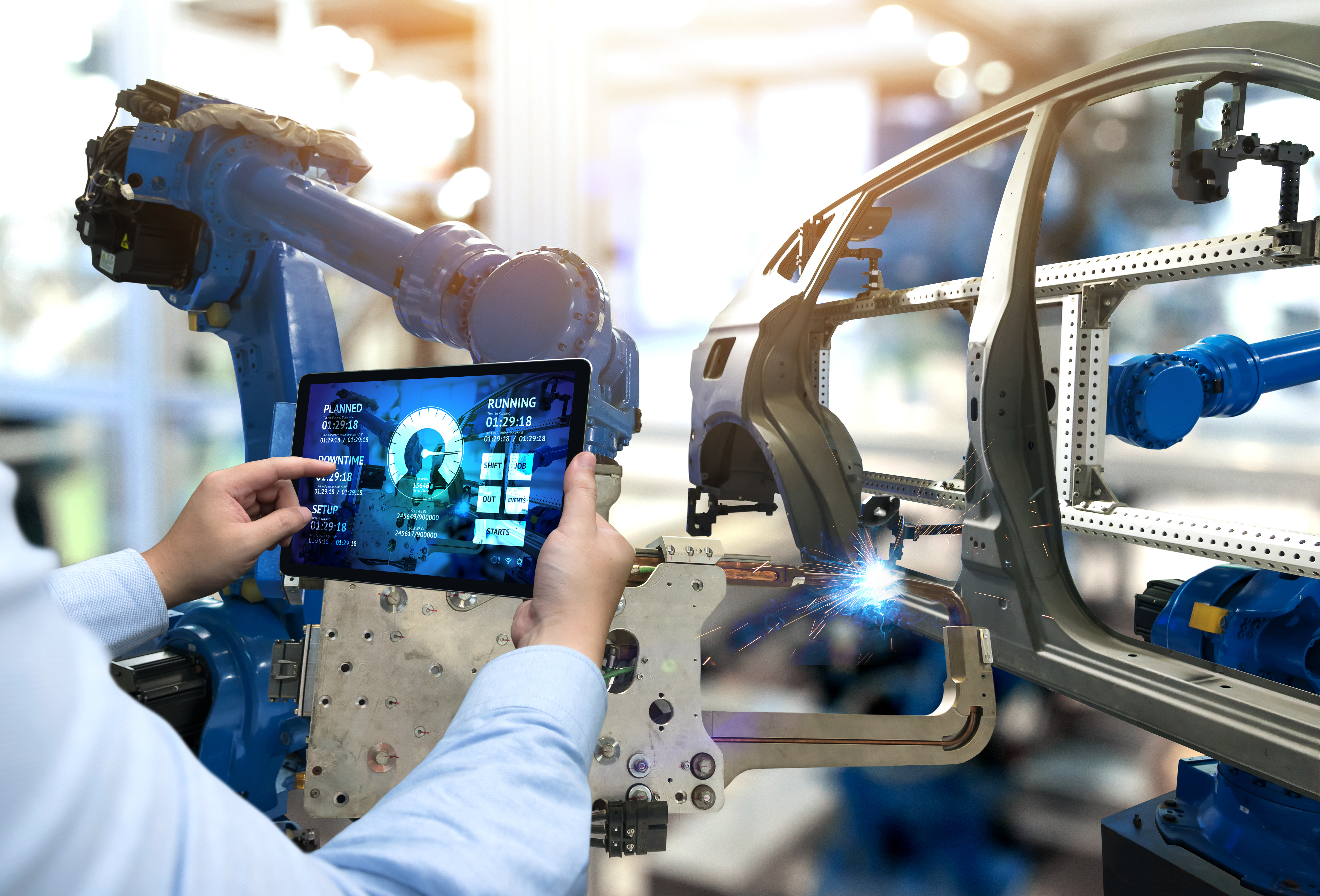 A photo of a person holding a tablet with graphs up to an assembly robot.