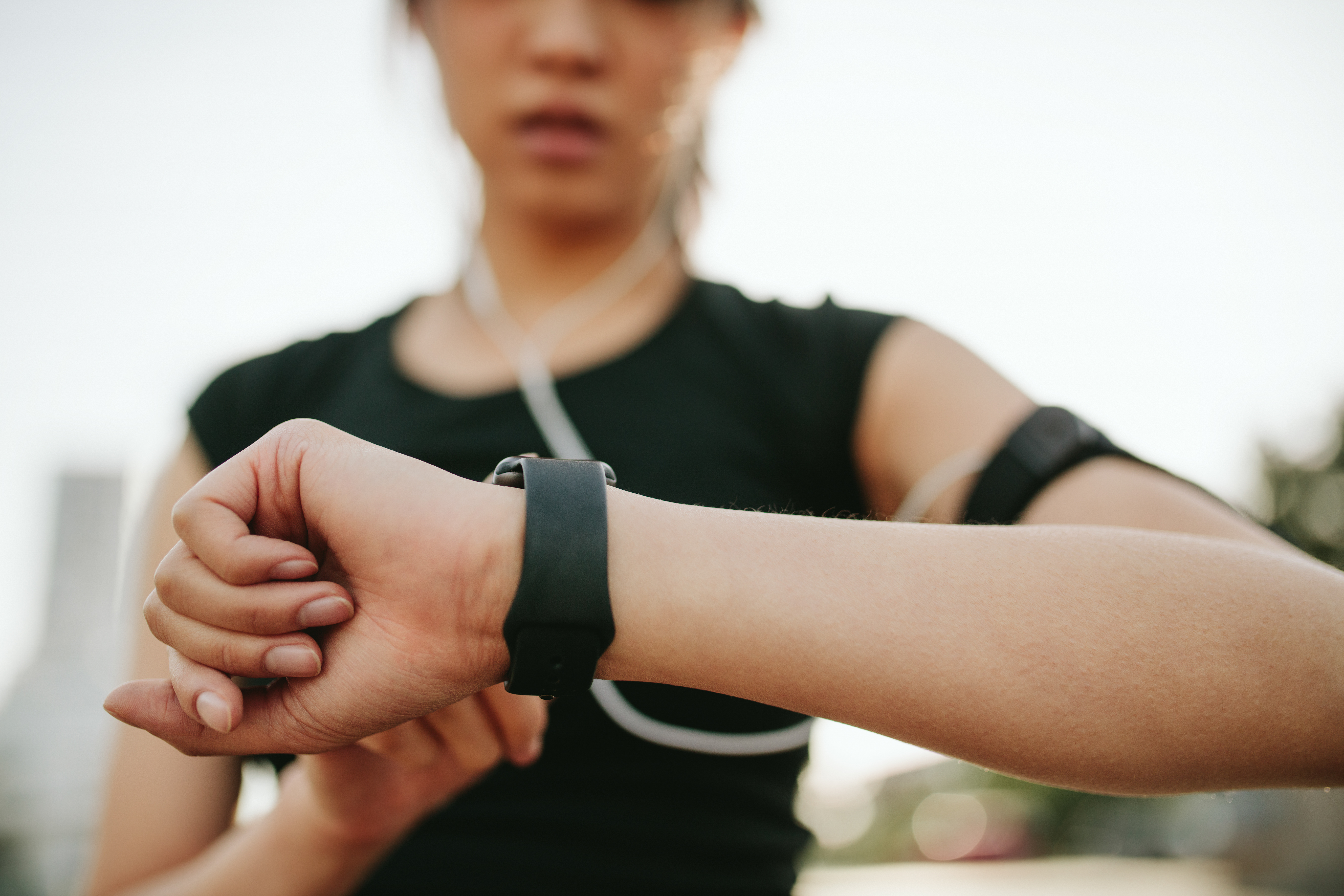 A jogger wearing headphones is looking at her watch.