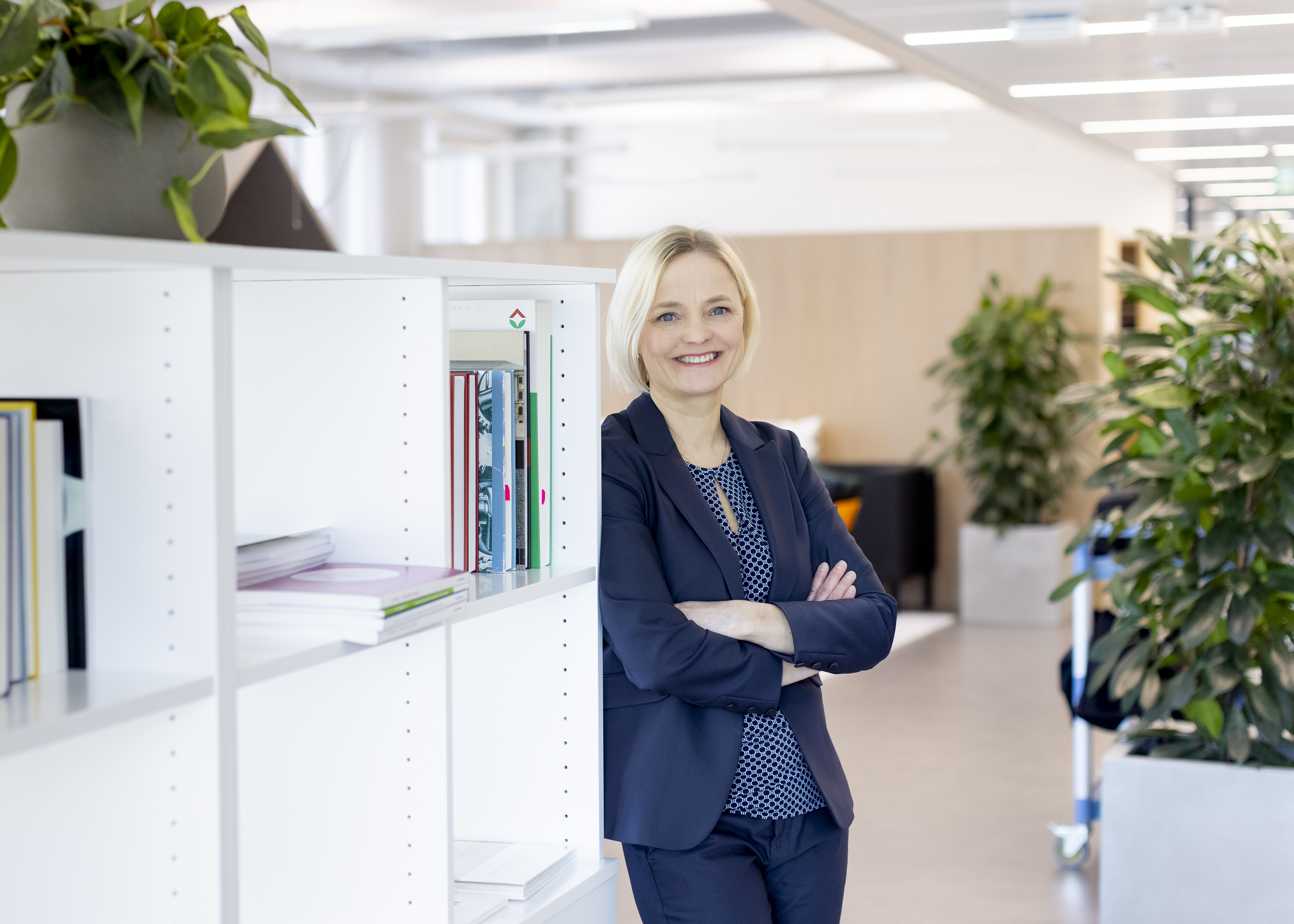 Peppi Härme katsoo hymyillen kameraan ja nojaa kirjahyllyyn.