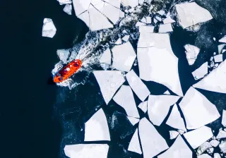 Ilmakuva laivasta, joka ajaa jäälohkareiden läpi.