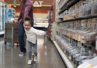 A child is excitedly pulling their parent towards the candy aisle inside a grocery store