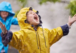 Two children are playing in the rain while the child in front is catching rain drops in their mouth
