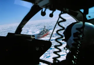 A shot from inside a helicopter shows the pilot overlooking an icebreaker ship going through ice in arctic conditions