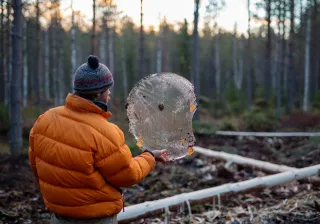 A man is lifting á round piece of ice and looking through it in a forest
