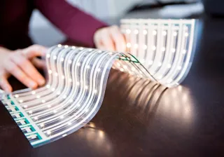A piece of bent, flexible LED foil is illuminated and laid out on a table