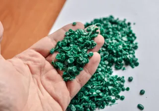 A close up photo of a hand holding up green recycled plastic chips.