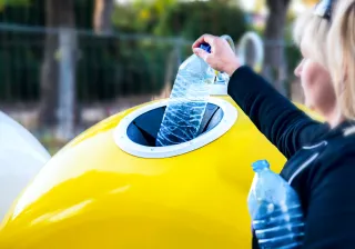 A photo of a person putting plastic bottles into a recycling bin.