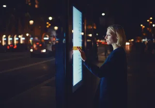 A photo of a person using a touch screen information board in a dark city setting.