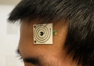 A squareshaped patch with electronic circuits attached to a person&#039;s forehead.