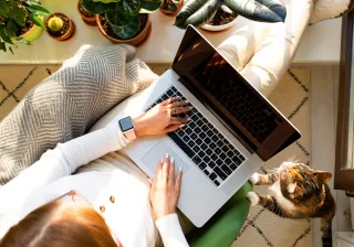 A woman working on a laptop with a cat by her side