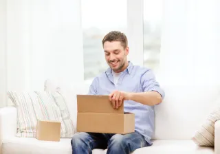 Mies istuu valkealla sohvalla ja avaa pahvilaatikkoa