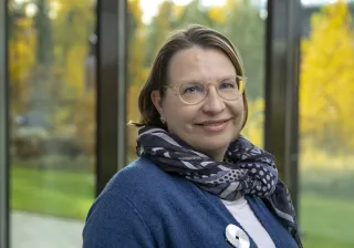 Tiina Nakari Setälä smiling at the camera, she is wearing glasses and a blue cardigan