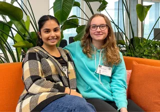 Maia and Sylvi sitting on an orange couch at the VTT office and smiling at the camera