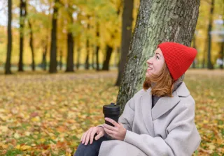A woman sitting in a forest holding a recyclable cup
