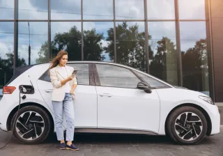 a woman charging an electric car while on her mobile phone