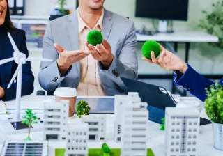 Trio of businesspeople, including a middleaged Asian man and woman, strategize at their desk, prioritizing sustainability renewable energy adoption, waste reduction, and ecofriendly practices.