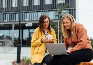 Two VTTers in front of VTT FutureHub with a laptop.