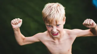 A child is cleching their fists and making a tough pose while grimacing
