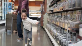 A child is excitedly pulling their parent towards the candy aisle inside a grocery store