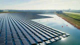 A large amount or solar panels are floating on water used for irrigation in front of rows of greenhouses