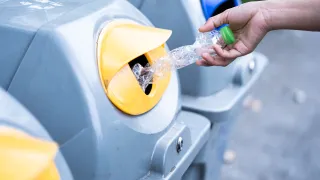 Hand inserting plastic bottle into recycling bin