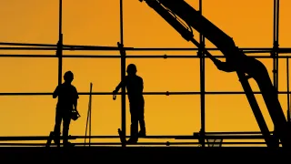 Two construction workers standing against yellow sky.
