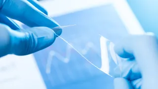 scientist hold in fingers small piece of transparent material