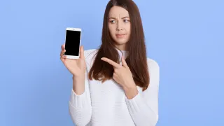 Nainen pitää kädessään älypuhelinta ja näyttää huolestuneelta
