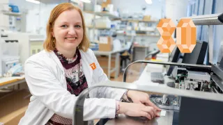 Liisa Hakola at the lab, smiling at the camera, holding a bluegreen algae test