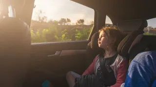 Lapsi istuu auton takapenkillä ja katselee haaveillen ulos auton ikkunasta.