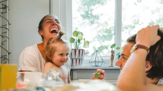 A family of two adults and a small child are sitting in the kitchen, laughing