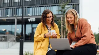 Two VTTers in front of VTT FutureHub with a laptop.