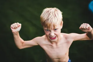 A child is cleching their fists and making a tough pose while grimacing
