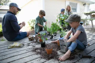 A family is sitting on a deck potting plants together