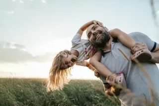 A girl is sitting on her father&#039;s shoulders, playing and laughing in a field at sunset