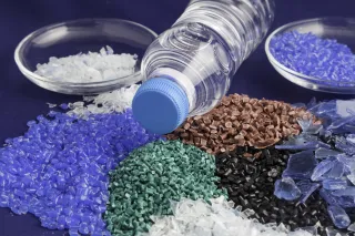A photo of a plastic bottle surrounded by different colored plastic pellets.