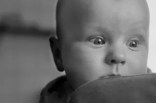 Black and white photo of baby looking curiously over its parent&#039;s shoulder