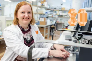 Liisa Hakola at the lab, smiling at the camera, holding a bluegreen algae test